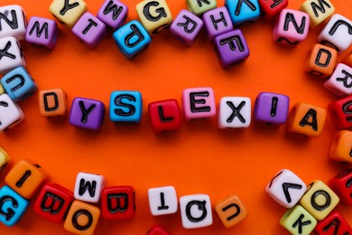 Colorful beads with word Dyslexia on orange background, flat lay