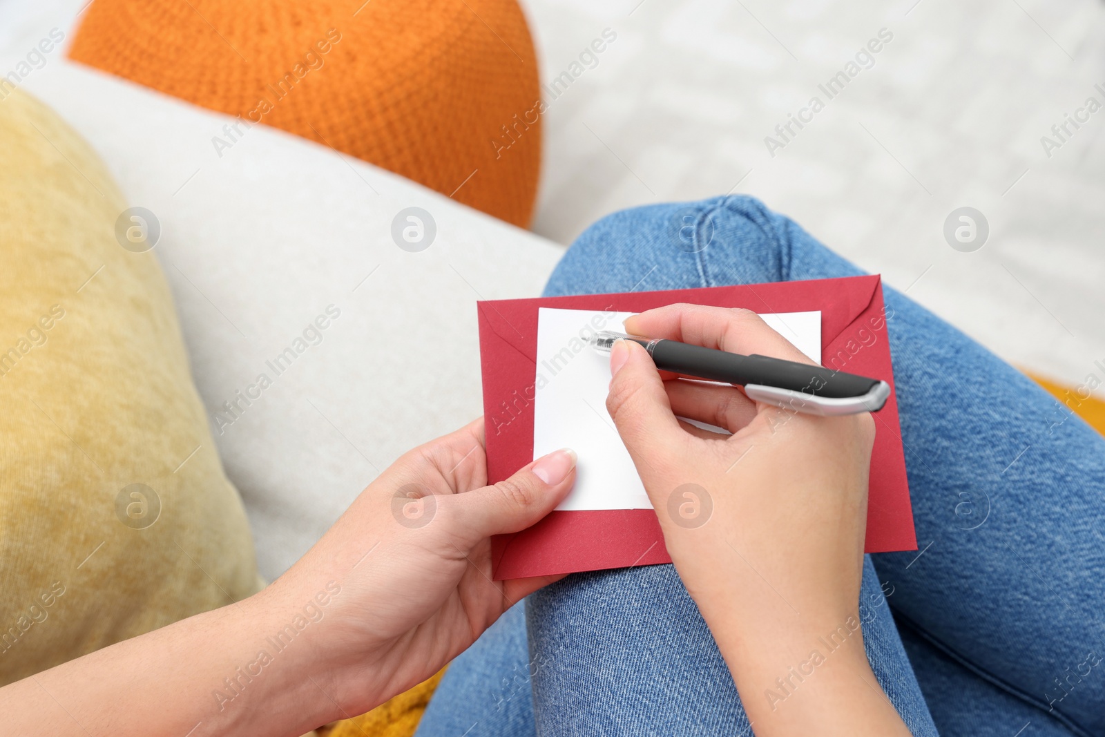 Photo of Young woman writing message in greeting card on sofa, above view