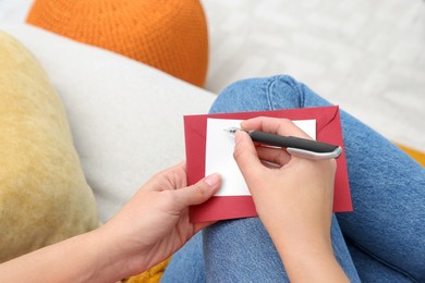 Photo of Young woman writing message in greeting card on sofa, above view