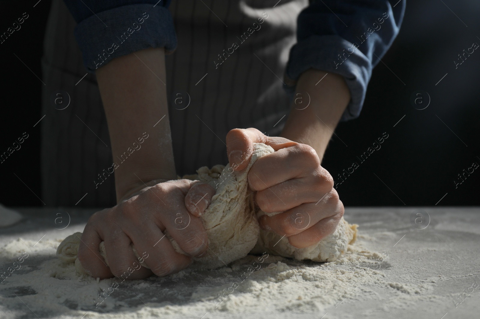 Photo of Making bread. Woman kneading dough at table on dark background, closeup