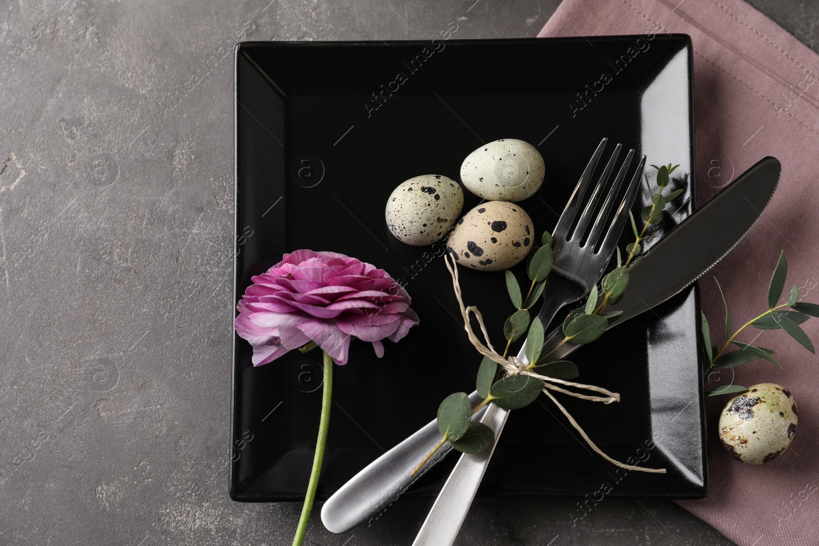 Photo of Festive Easter table setting with quail eggs and floral decoration on dark background, flat lay