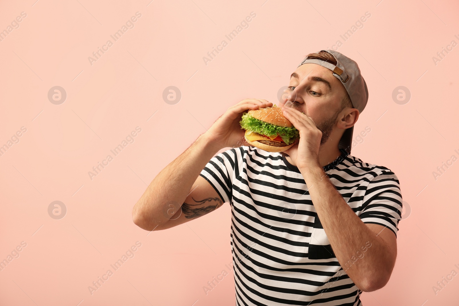 Photo of Young man eating tasty burger on color background. Space for text