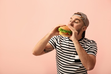 Young man eating tasty burger on color background. Space for text