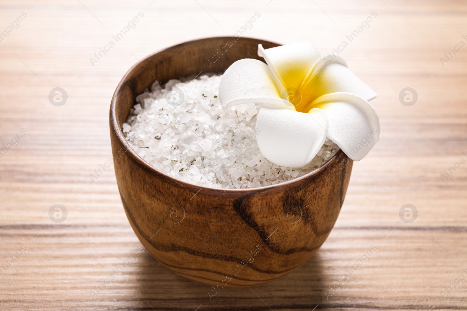 Photo of White sea salt for spa scrubbing procedure and flower on wooden table