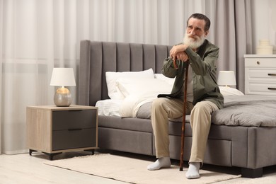 Photo of Senior man with walking cane on bed at home