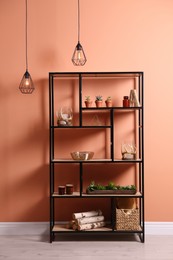 Photo of Shelving with different decor, houseplants and firewood near coral wall. Interior design
