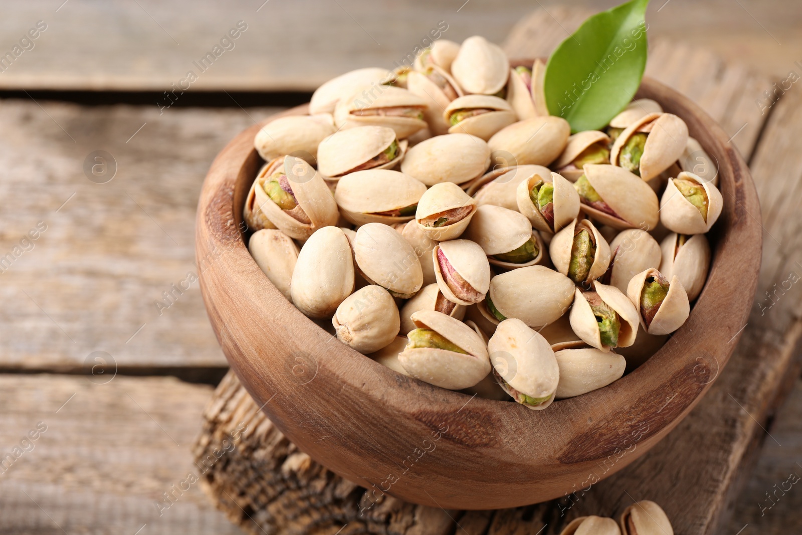 Photo of Delicious pistachios in bowl on wooden table, closeup