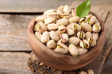 Photo of Delicious pistachios in bowl on wooden table, closeup