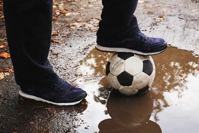 Photo of Man with soccer ball in muddy puddle outdoors, closeup