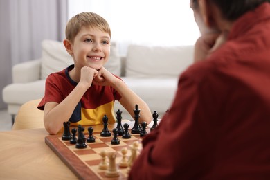 Photo of Little boy playing chess with his grandfather at table in room