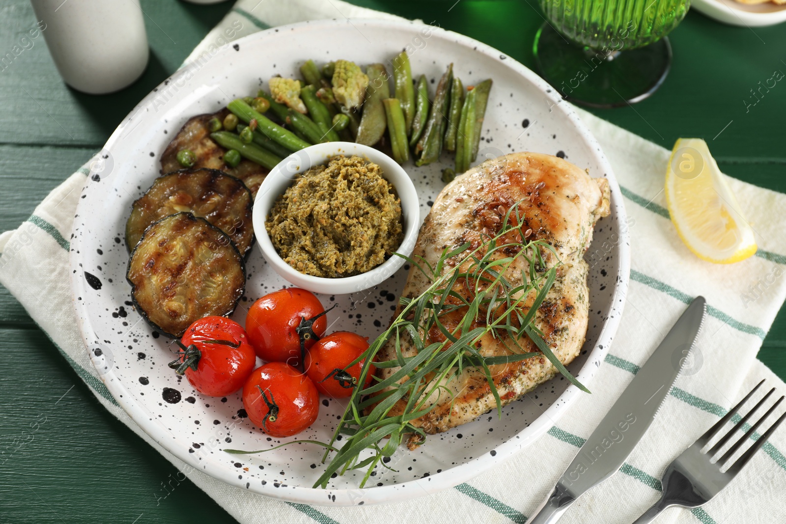 Photo of Tasty chicken, vegetables with tarragon and pesto sauce served on green wooden table, above view