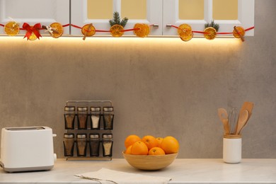 Photo of Handmade garland from dry orange slices and fir branches hanging on cabinets in kitchen