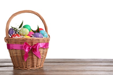 Photo of Colorful Easter eggs in wicker basket on wooden table against white background