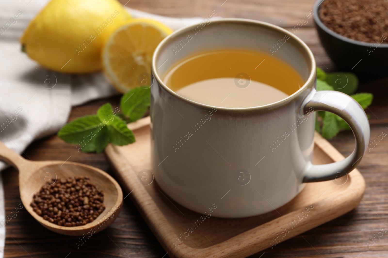 Photo of Cup of aromatic buckwheat tea and spoon with granules on wooden table, closeup