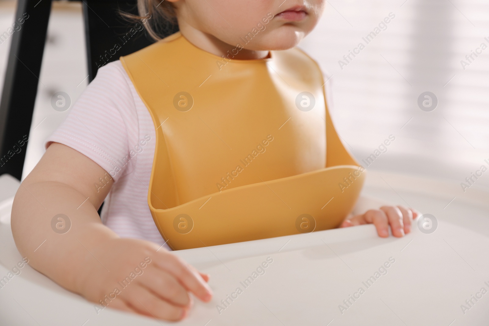 Photo of Cute little baby wearing bib in highchair at home, closeup