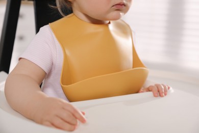 Photo of Cute little baby wearing bib in highchair at home, closeup