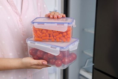 Photo of Woman holding containers with different fresh products near fridge, closeup. Food storage