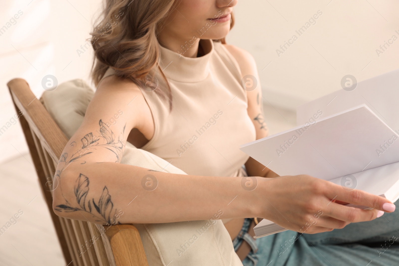 Photo of Beautiful woman with tattoos on arms reading book at home, closeup