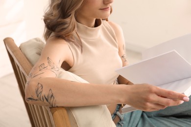 Photo of Beautiful woman with tattoos on arms reading book at home, closeup