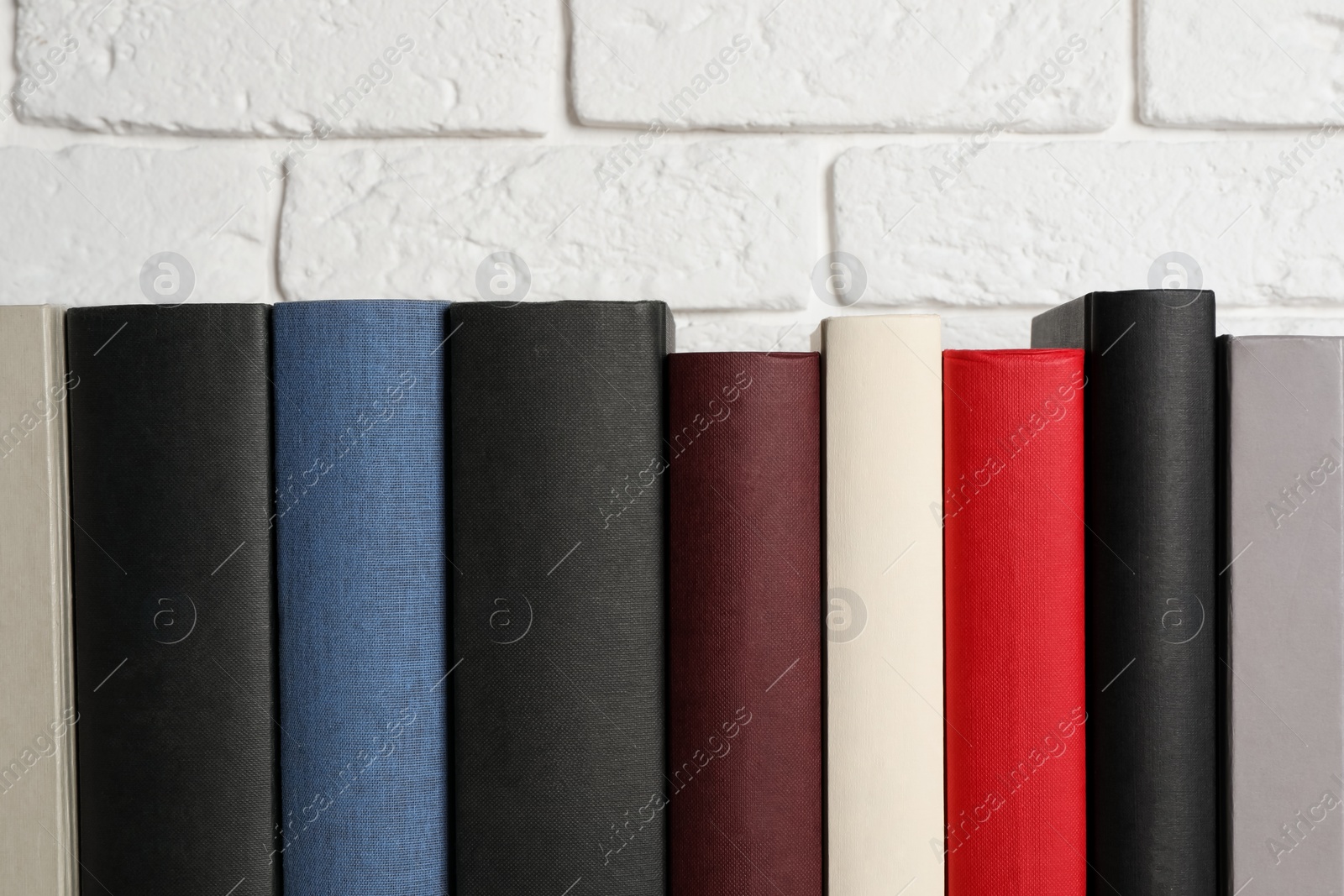 Photo of Many different hardcover books near white brick wall, space for text