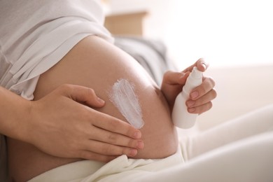 Photo of Young pregnant woman with cosmetic product indoors, closeup