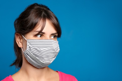 Young woman in protective face mask on blue background, space for text