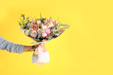 Photo of Man holding beautiful flower bouquet on yellow background, closeup view. Space for text