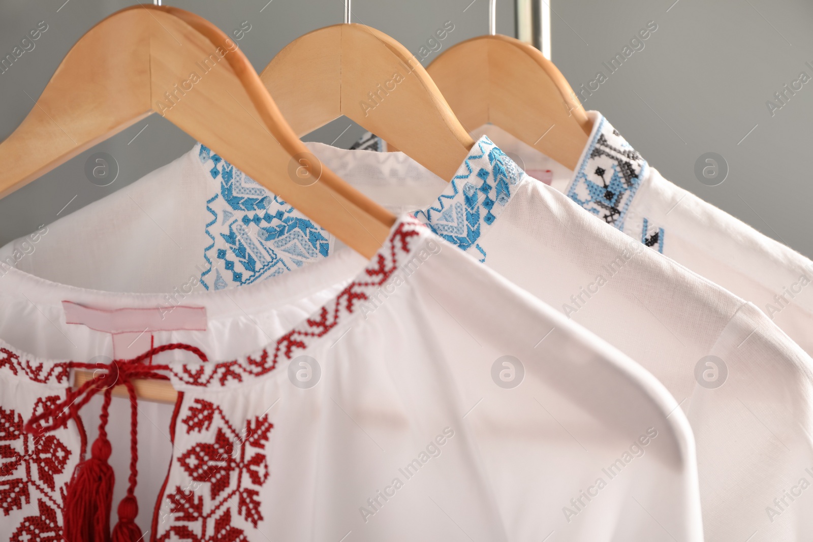 Photo of Beautiful shirts with different embroidery designs hanging on grey background, closeup. Ukrainian national clothes