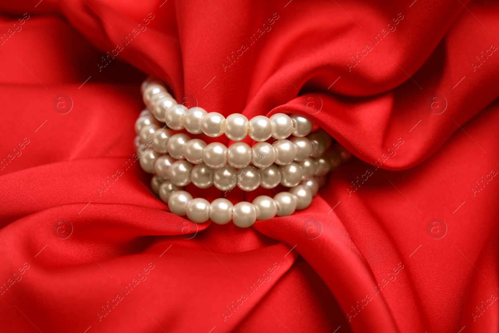 Photo of Beautiful pearls with red silk as background, closeup