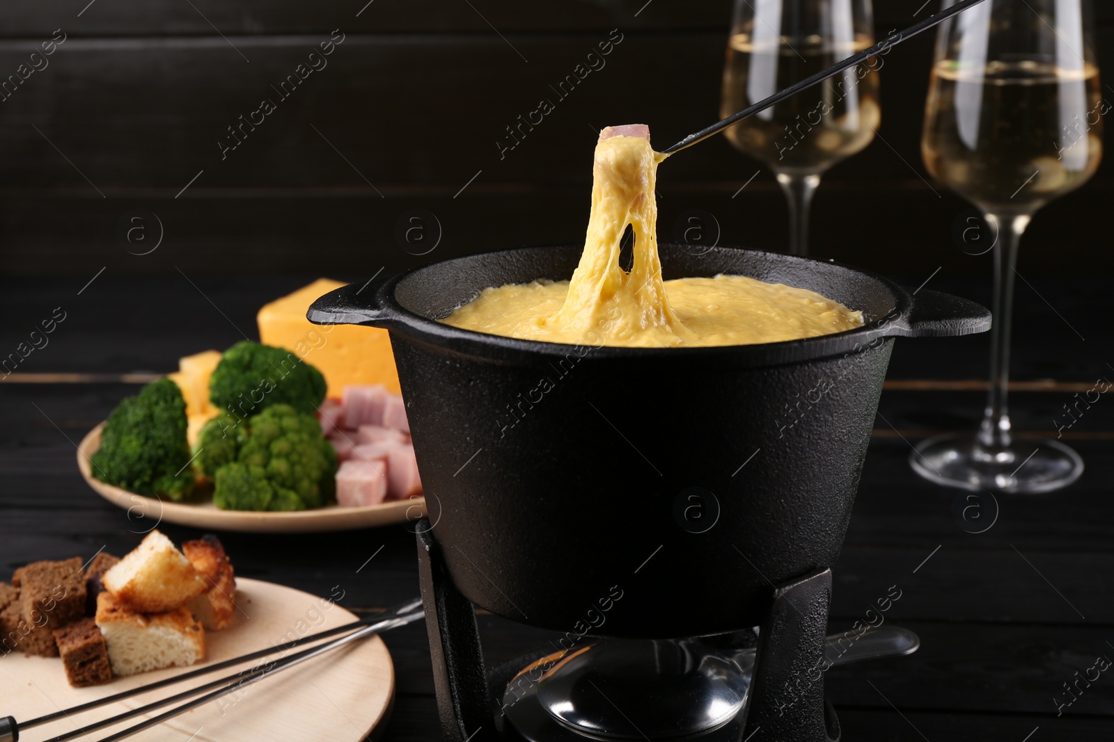 Photo of Dipping piece of ham into fondue pot with melted cheese on table