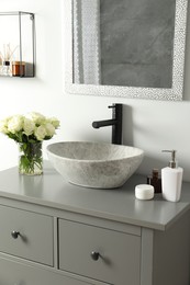 Photo of Vase with beautiful white roses and toiletries near sink in bathroom