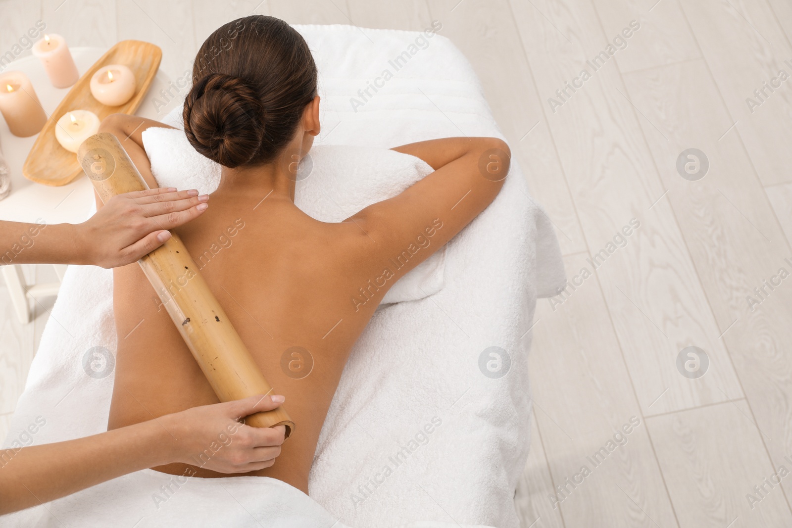 Photo of Young woman having massage with bamboo stick in wellness center