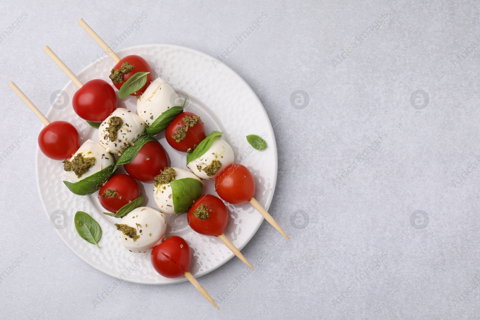 Photo of Caprese skewers with tomatoes, mozzarella balls, basil and pesto sauce on white table, top view. Space for text