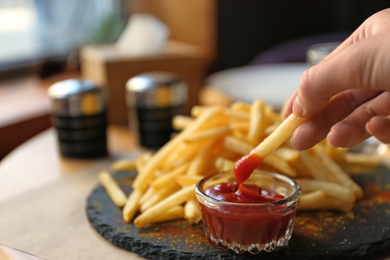 Photo of Woman dipping French fries into red sauce in cafe, closeup