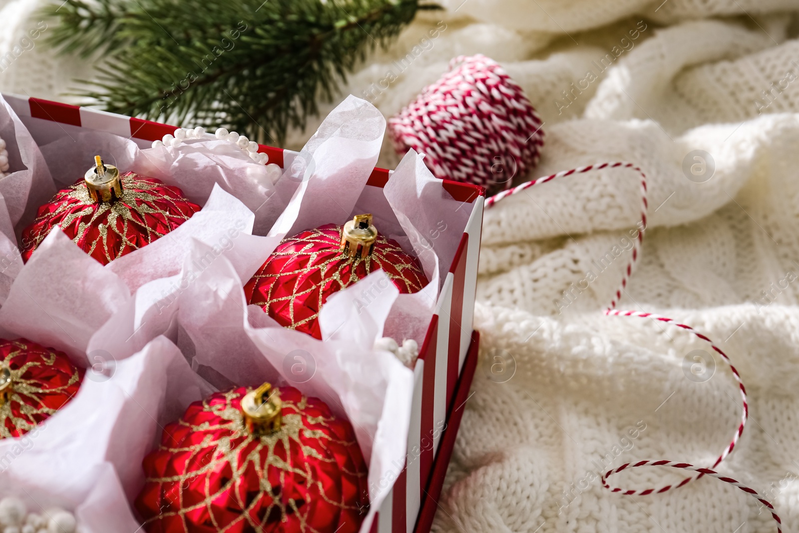 Photo of Beautiful red Christmas baubles in box on knitted plaid, closeup