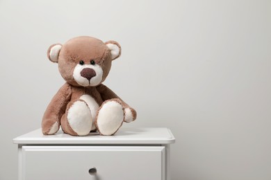 Photo of Cute teddy bear on cabinet near light wall, space for text
