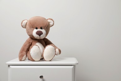 Cute teddy bear on cabinet near light wall, space for text