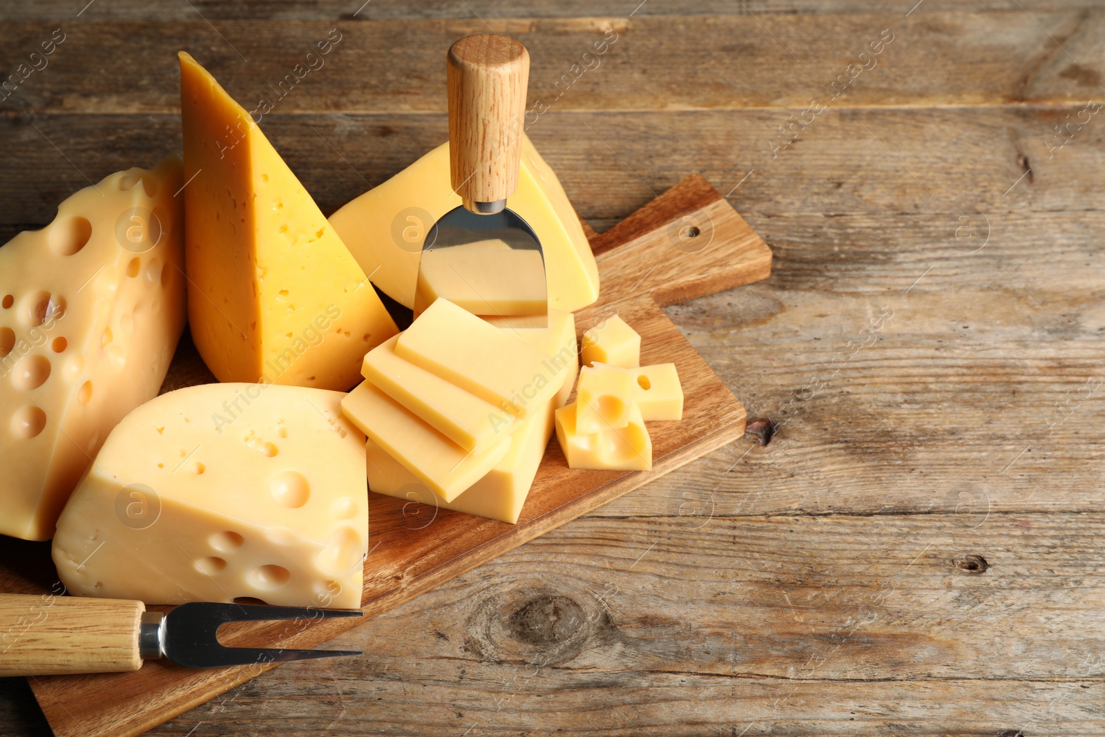 Photo of Different sorts of cheese, fork and knife on wooden table. Space for text