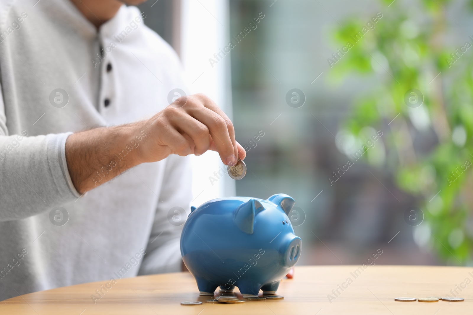 Photo of Man putting money into piggy bank at table, closeup. Space for text