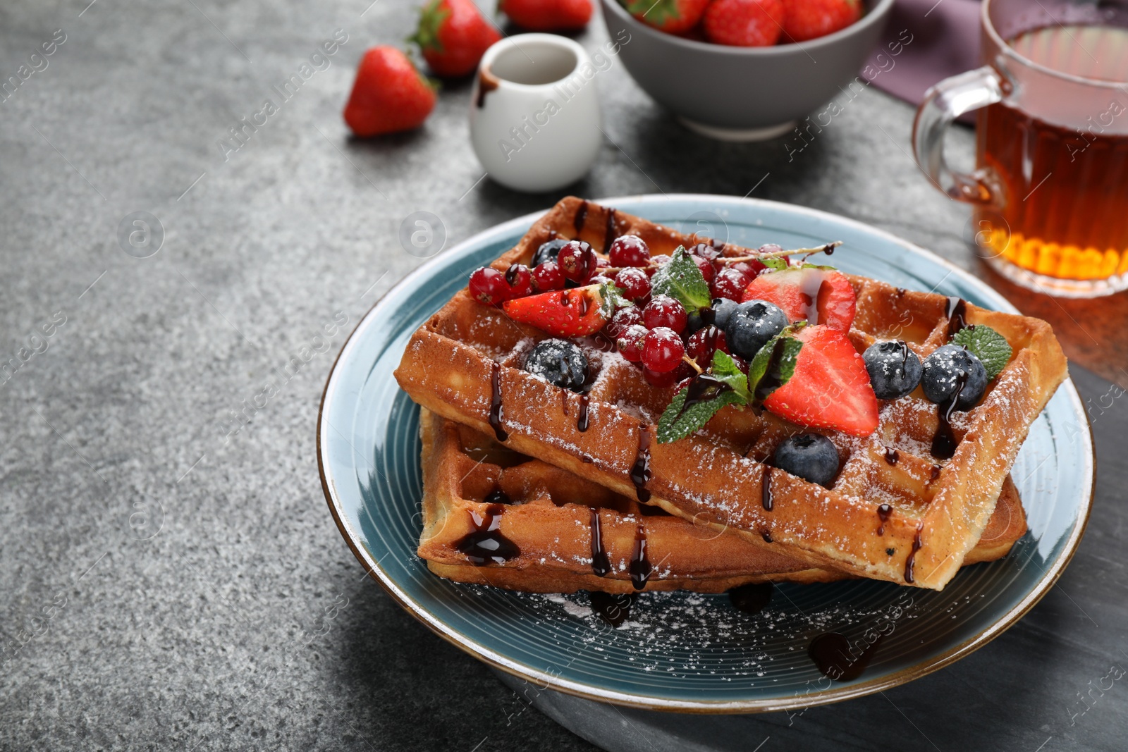 Photo of Delicious Belgian waffles with berries served on grey table