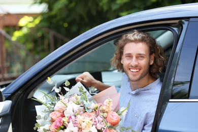 Photo of Young handsome man with beautiful flower bouquet in car