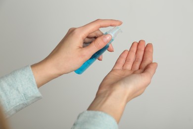 Woman applying antiseptic gel on light grey background, closeup