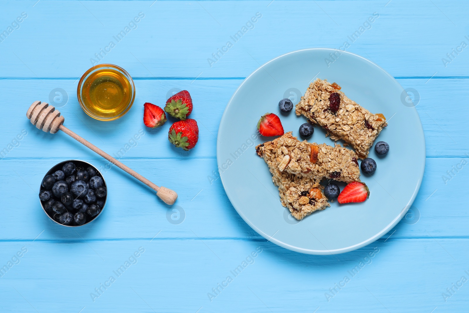 Photo of Tasty granola bars with berries and honey on light blue wooden table, flat lay