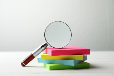 Photo of Magnifier glass and stack of colorful memory stickers on white wooden table, closeup. Find keywords concept