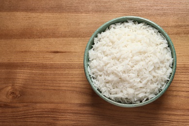 Photo of Bowl of tasty cooked rice on wooden background, top view. Space for text