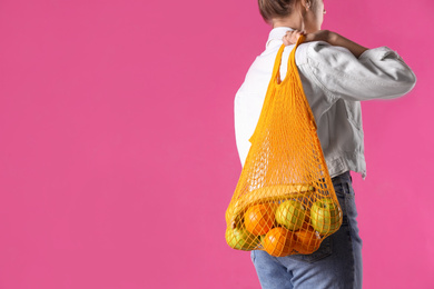 Photo of Woman holding net bag with fruits on pink background, closeup. Space for text