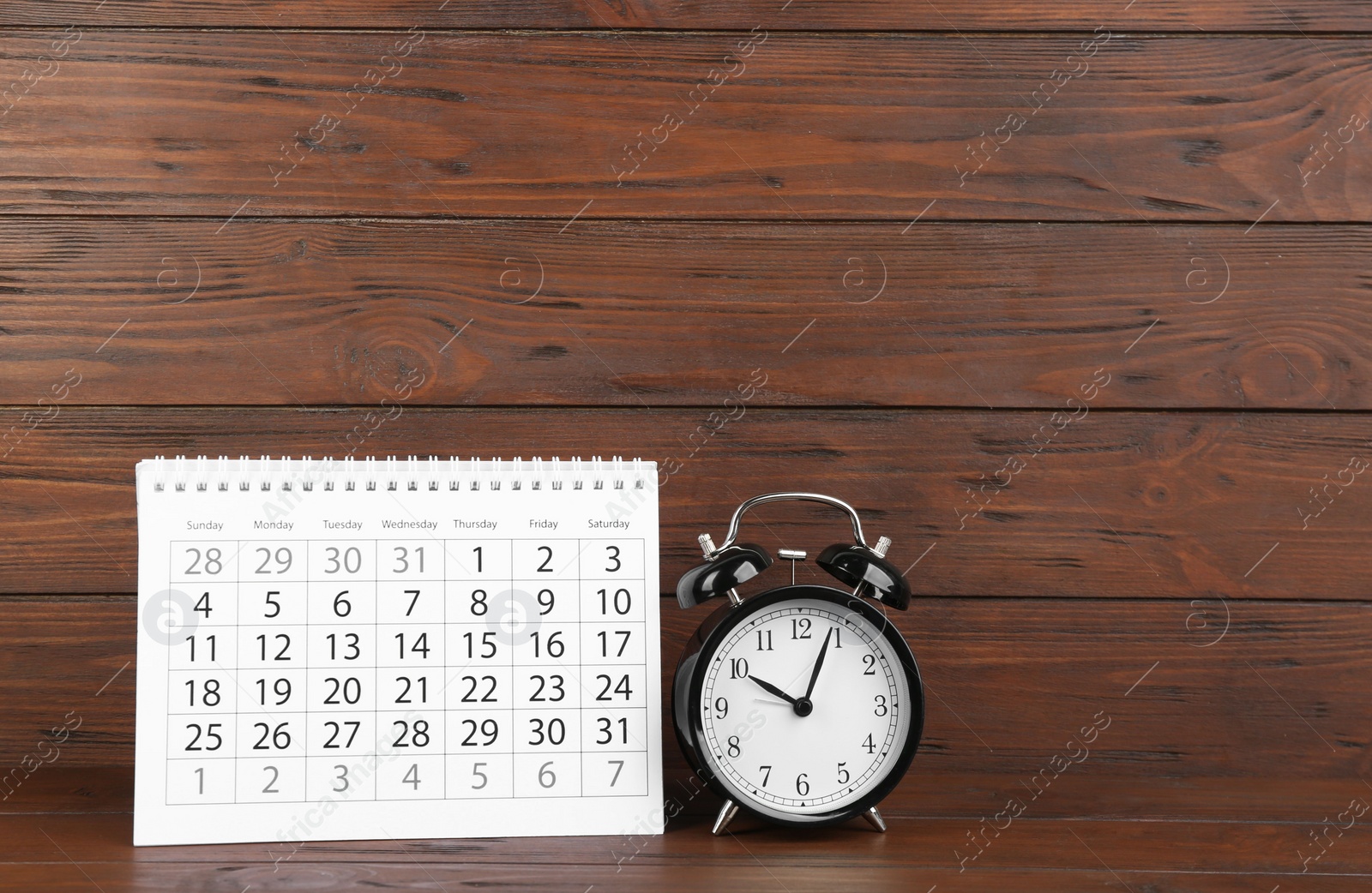 Photo of Calendar and alarm clock on wooden table