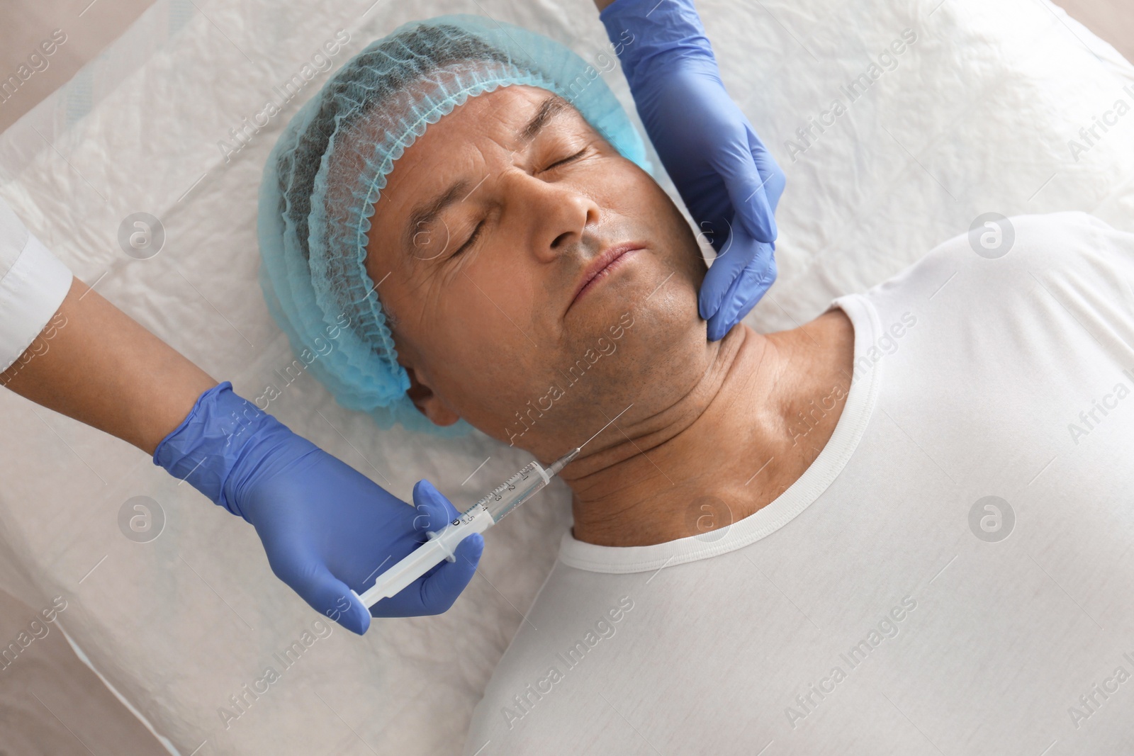 Photo of Mature man with double chin receiving injection in clinic, above view