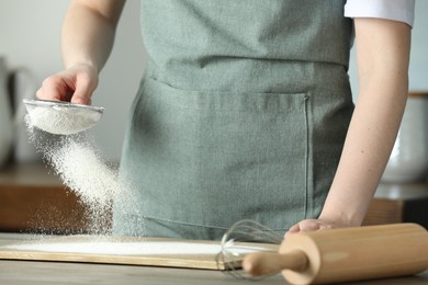 Woman sieving flour at table in kitchen, closeup