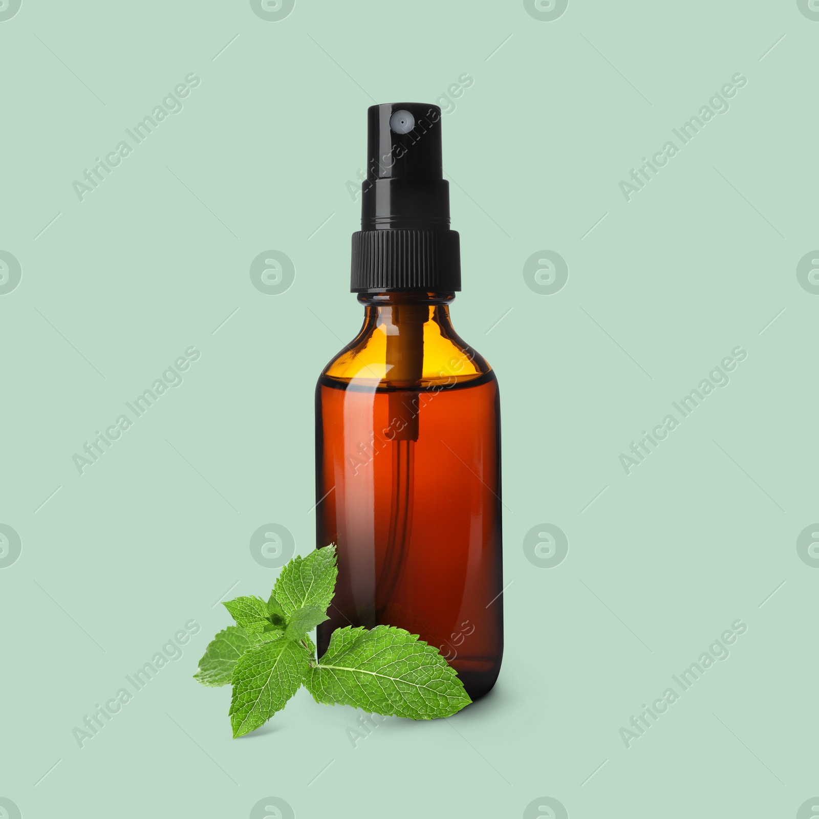 Image of Bottle of mint essential oil and leaves on pale light green background